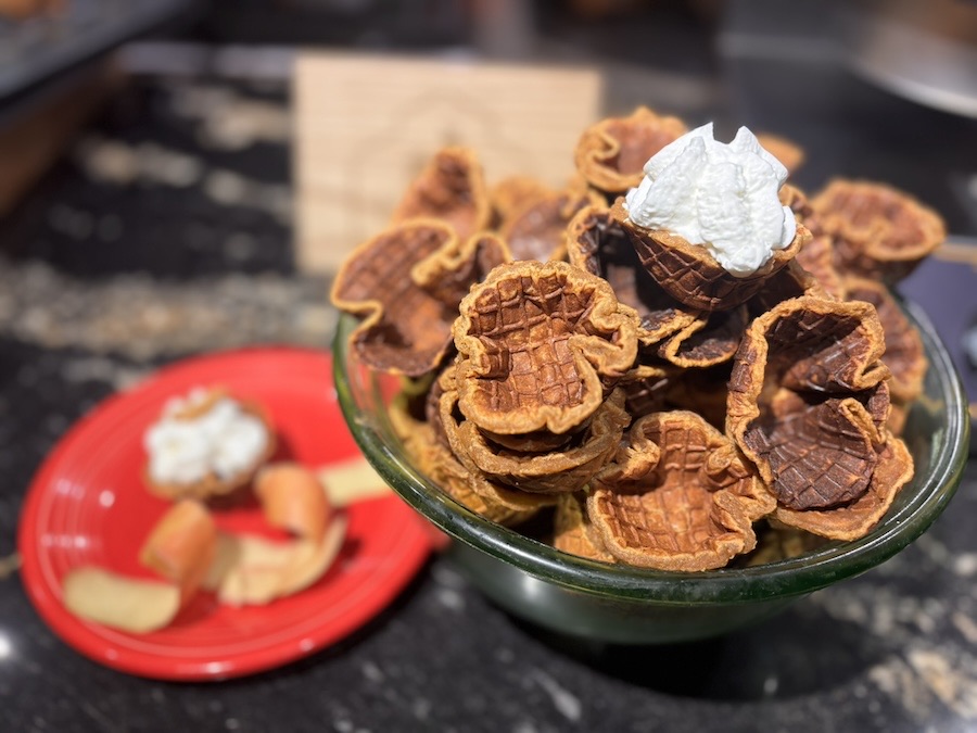 A glass bowl piled high with baked Apple Pup Cups, one topped with a swirl of whipped cream.